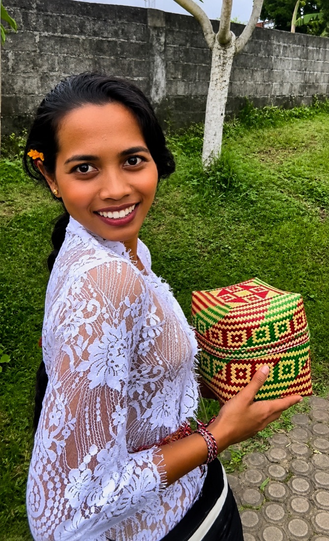 Ni Nyoman Ari Swarbudiani in a traditional Balinese lace kebaya, holding a hand-woven ceremonial box